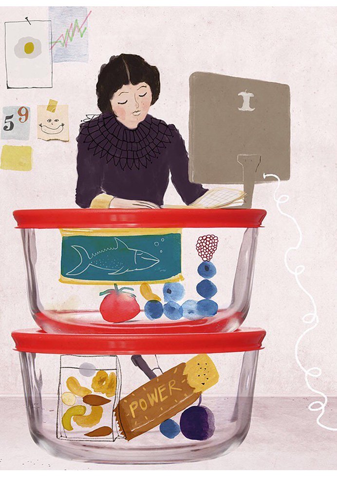 A woman works at her desk beside two glass meal-prep containers filled with healthy foods like fish, fruit, nuts and snacks.