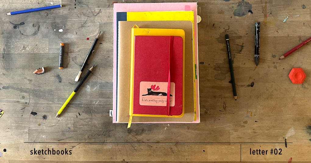 Several well-used sketchbooks stacked on a studio table, surrounded by pencils and drawing tools.